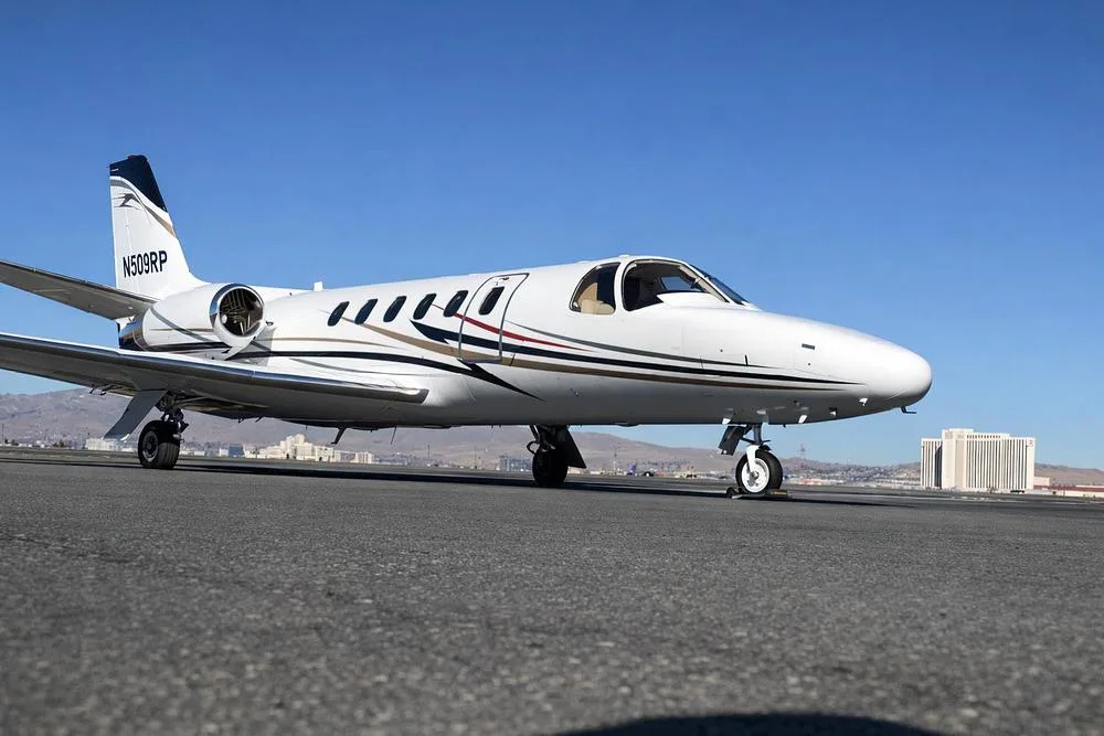 A white Cessna Citation jet with registration N509RP on the tail, parked on an airfield with distant buildings under a clear blue sky.