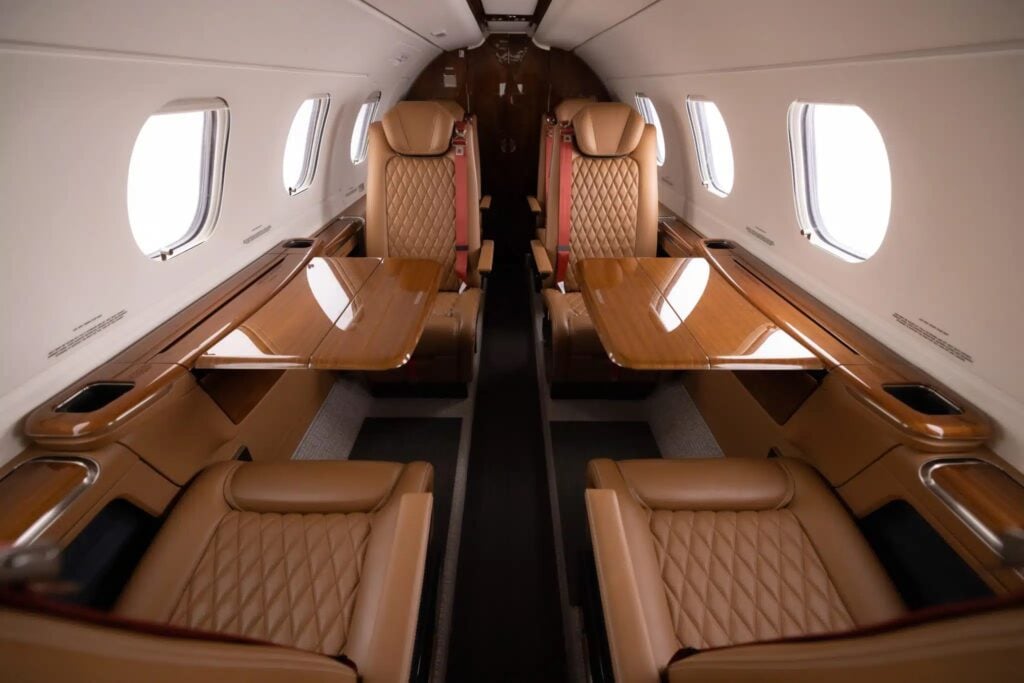 The interior of an aircraft with leather seats and wooden tables.