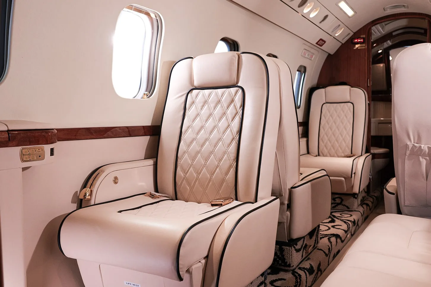 The luxurious interior of a private jet cabin with quilted cream leather seats and dark wood accents.