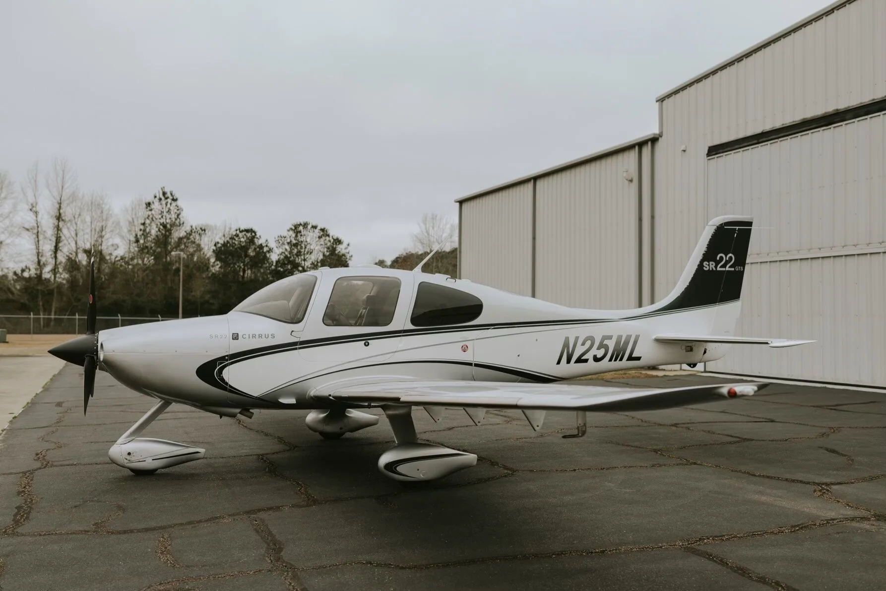 A side view of a silver Cirrus SR22 GTS aircraft with black and white stripes parked on an asphalt ramp.