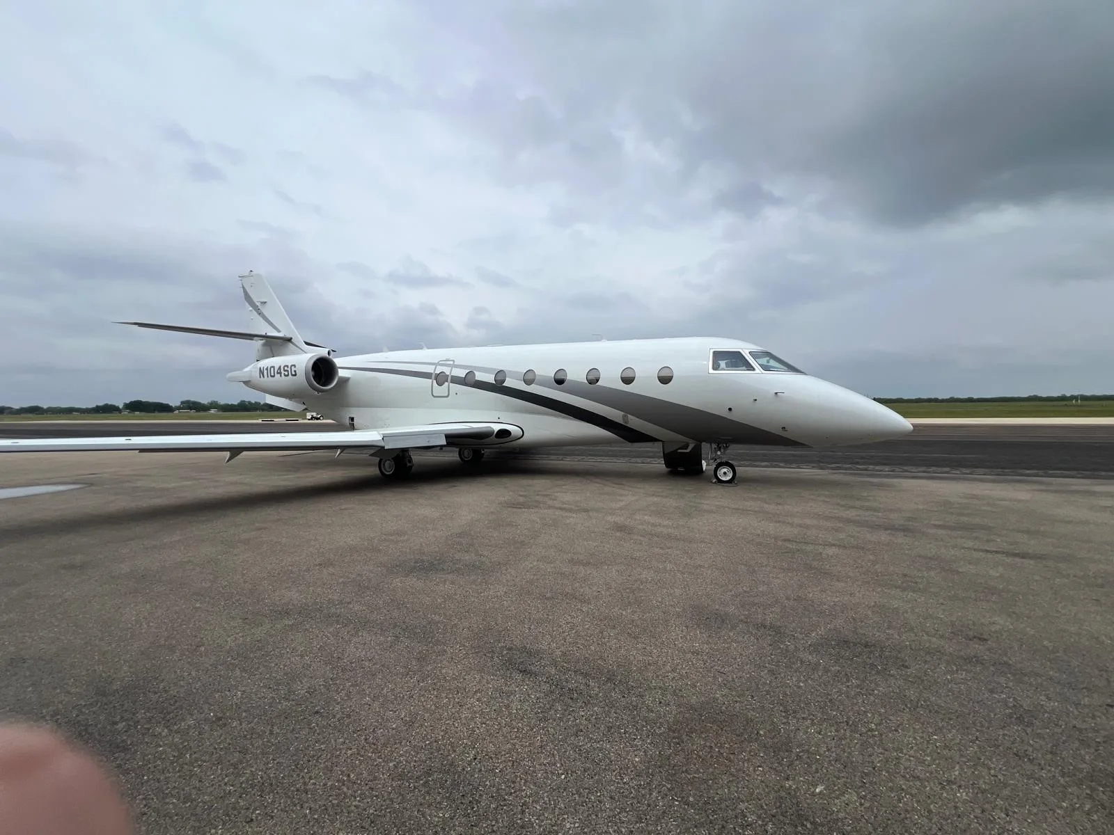 A white and gray jet with tail number N104SG sits on the tarmac under a cloudy sky.