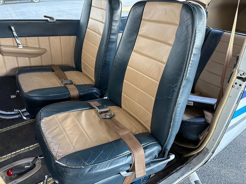 The front and rear two-tone blue and tan leather seats of an aircraft cabin, showing some wear on the upholstery.