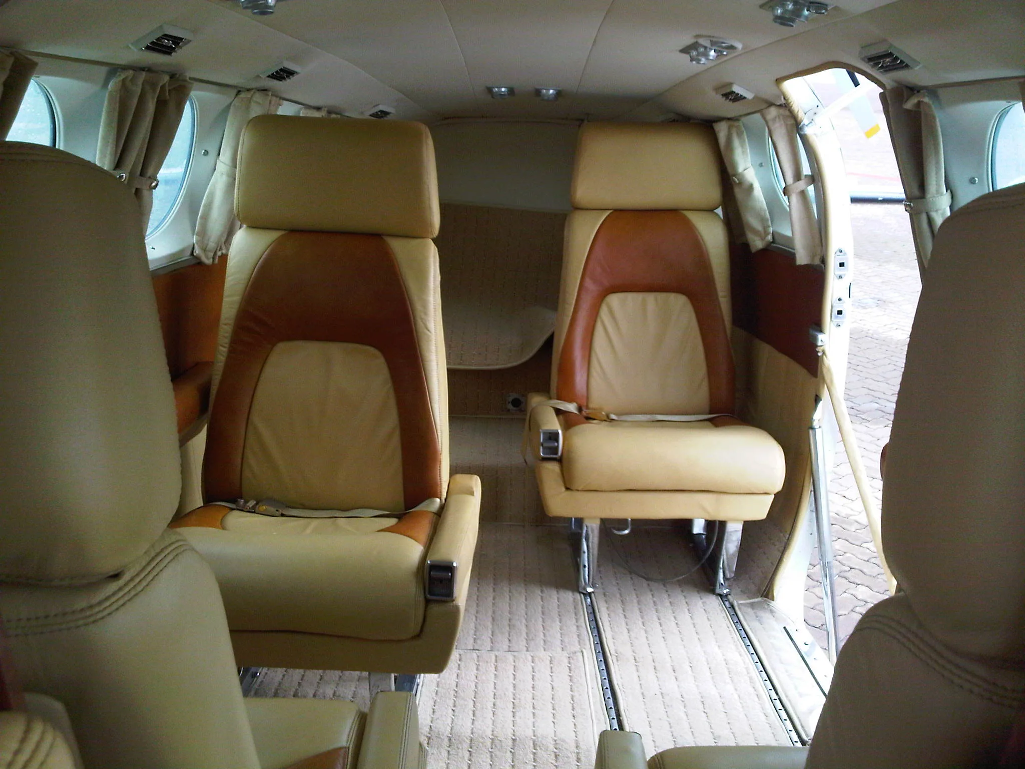 The aircraft cabin interior with two-tone tan and brown leather seats facing forward, with a carpeted floor.