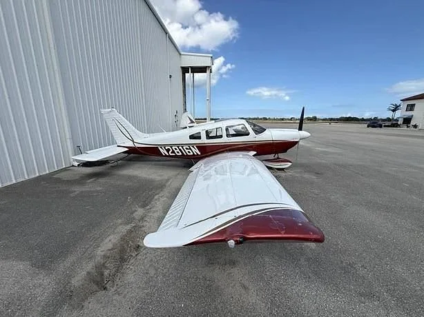 A white and red single-engine propeller aircraft with tail number N2816N parked next to a white hangar on an airfield.