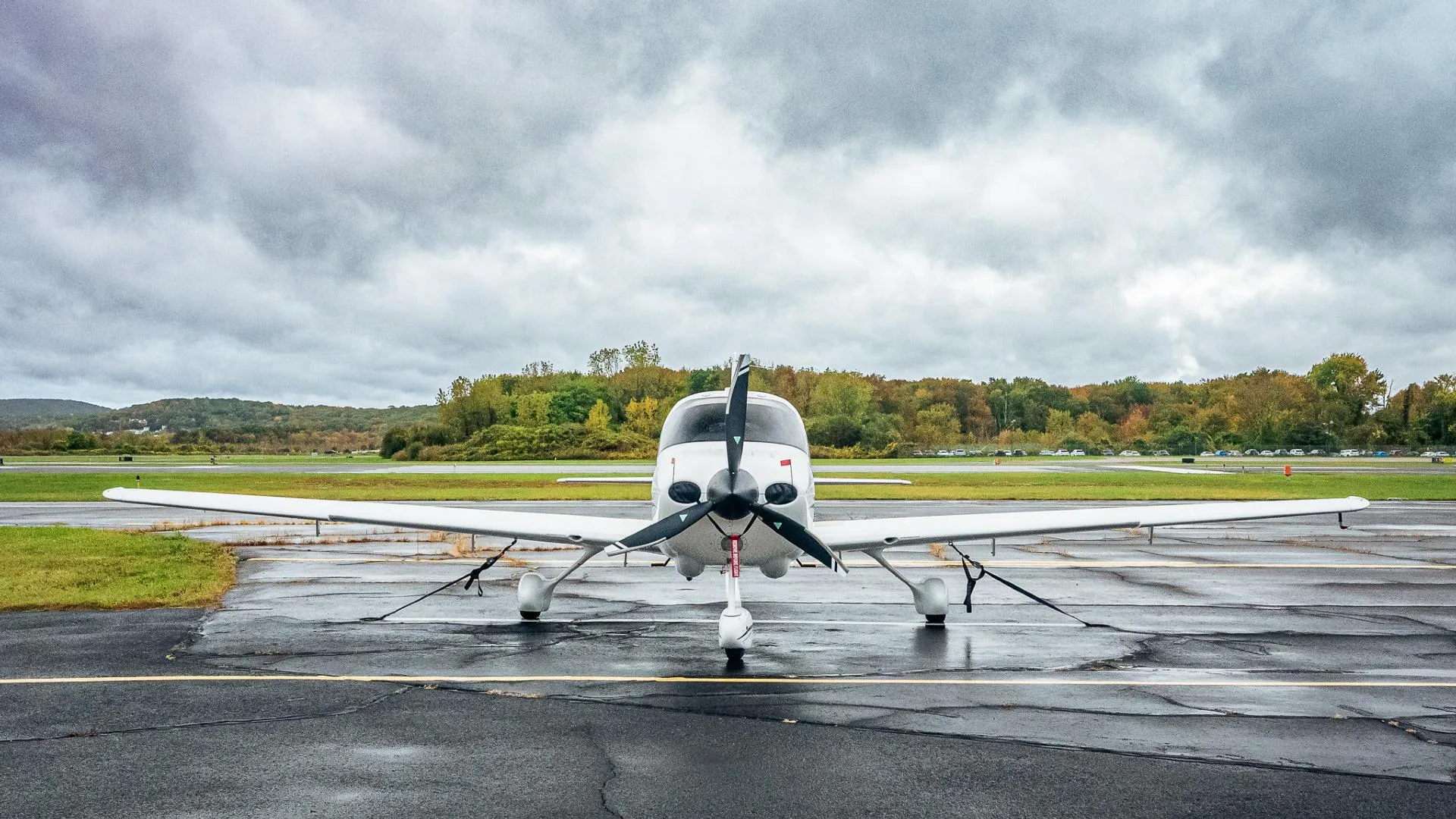 A head-on view of a white Cirrus SR20 aircraft with registration N899WT, parked on a wet tarmac under a cloudy sky.