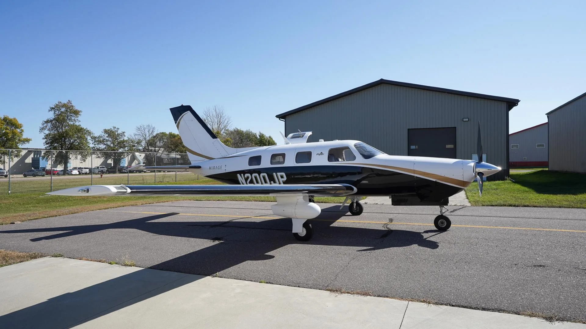 A side view of a white and black Piper Mirage N200JP with gold accents parked on an airfield.