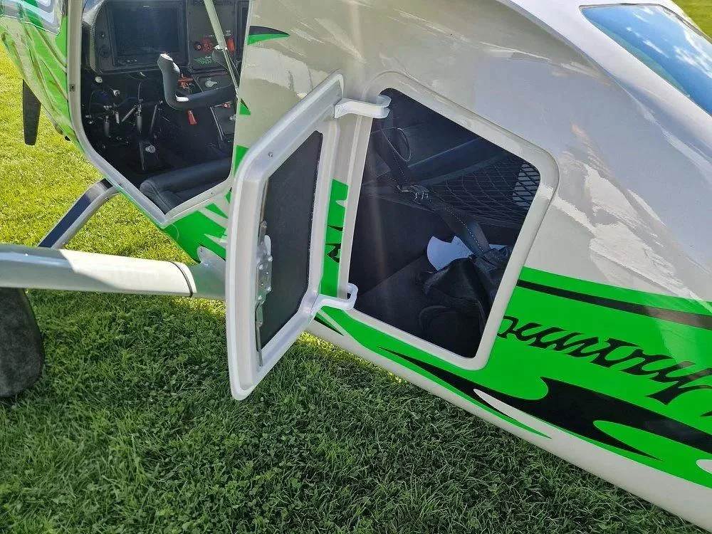 The side of a white and green Backcountry Super Cub aircraft with an open cargo door revealing a storage compartment.