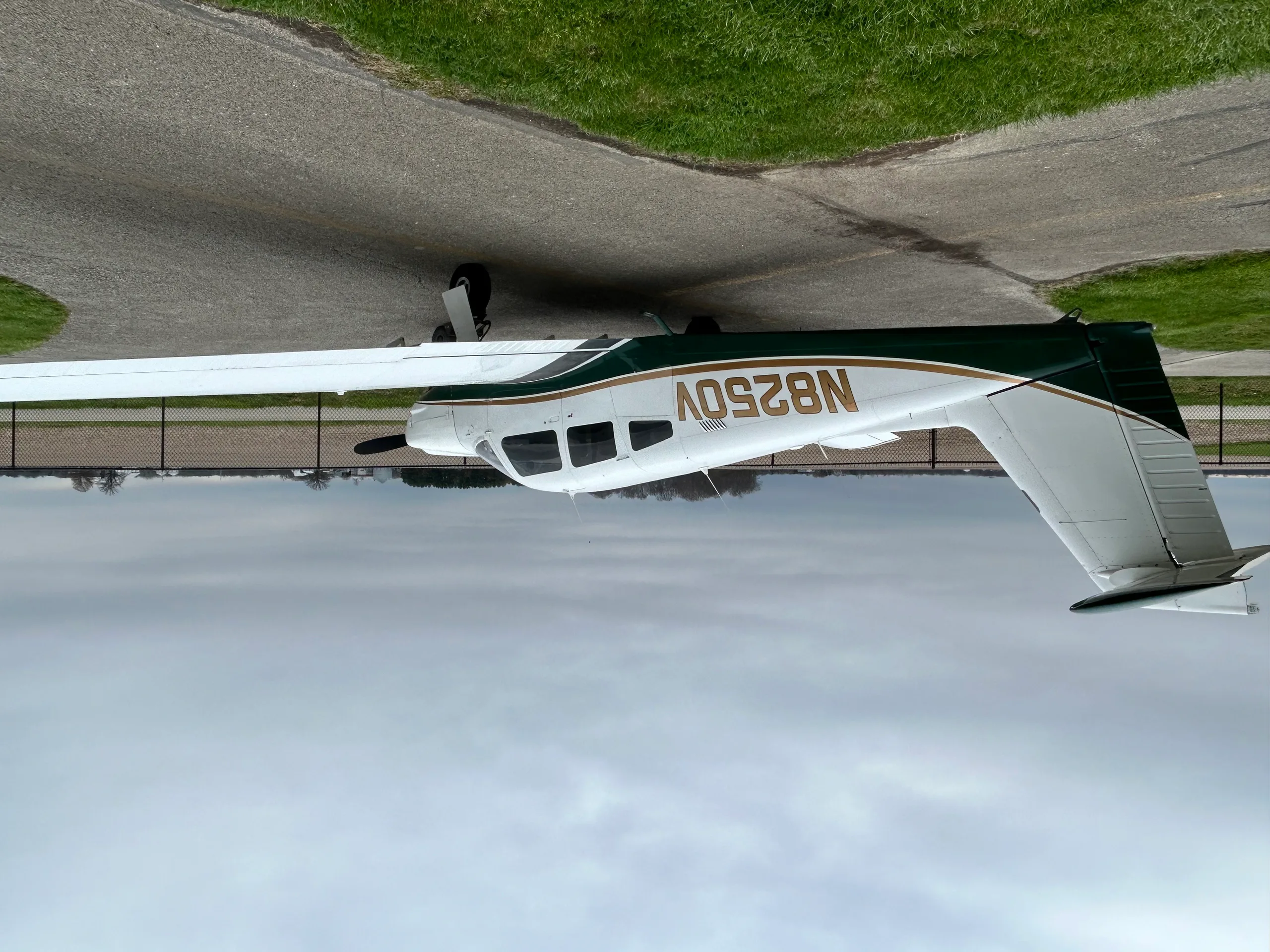A white and green single-engine aircraft, N8250V, parked on an asphalt taxiway under a cloudy sky.