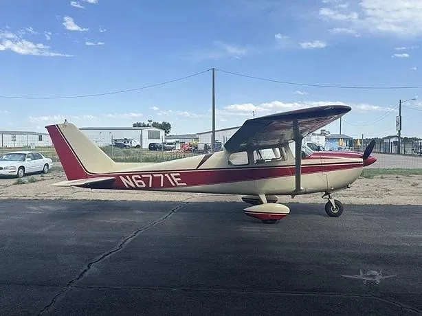 A Cessna 172 with a cream and red paint scheme, registration N6771E, parked on an asphalt ramp under a partly cloudy sky.