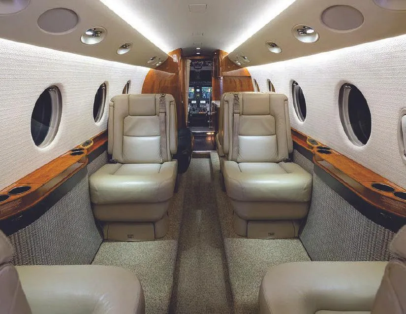 View of the aircraft cabin interior with tan leather seats and wood paneling, looking towards the front.