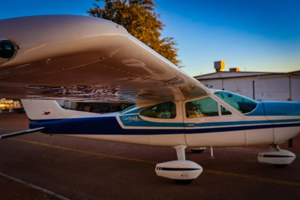 A side view of a white and blue Cessna 210 Centurion aircraft parked on a tarmac at sunset.