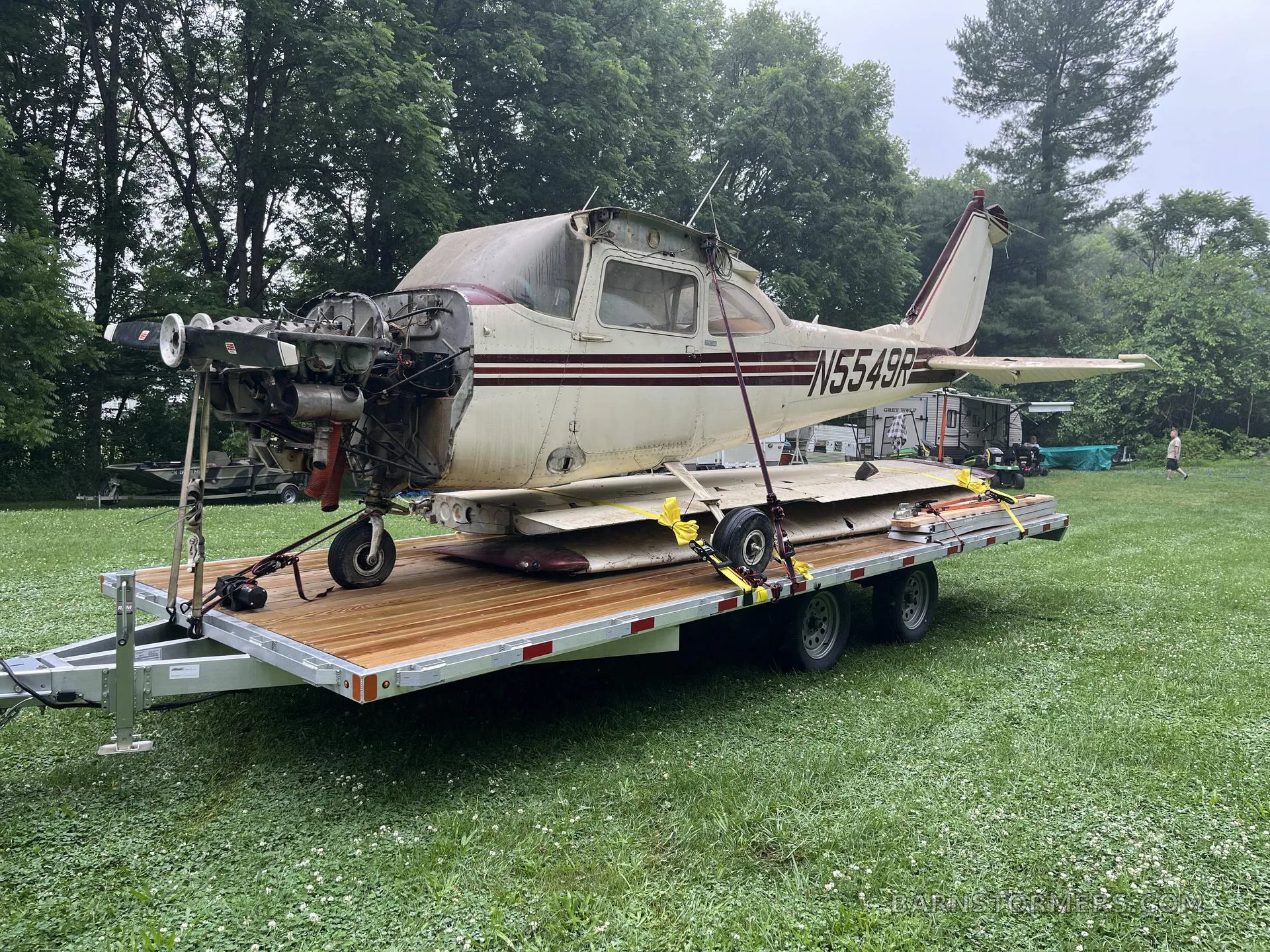 A disassembled white and maroon single-engine aircraft, registration N5549R, with its engine exposed, loaded on a wooden trailer in a grassy field.