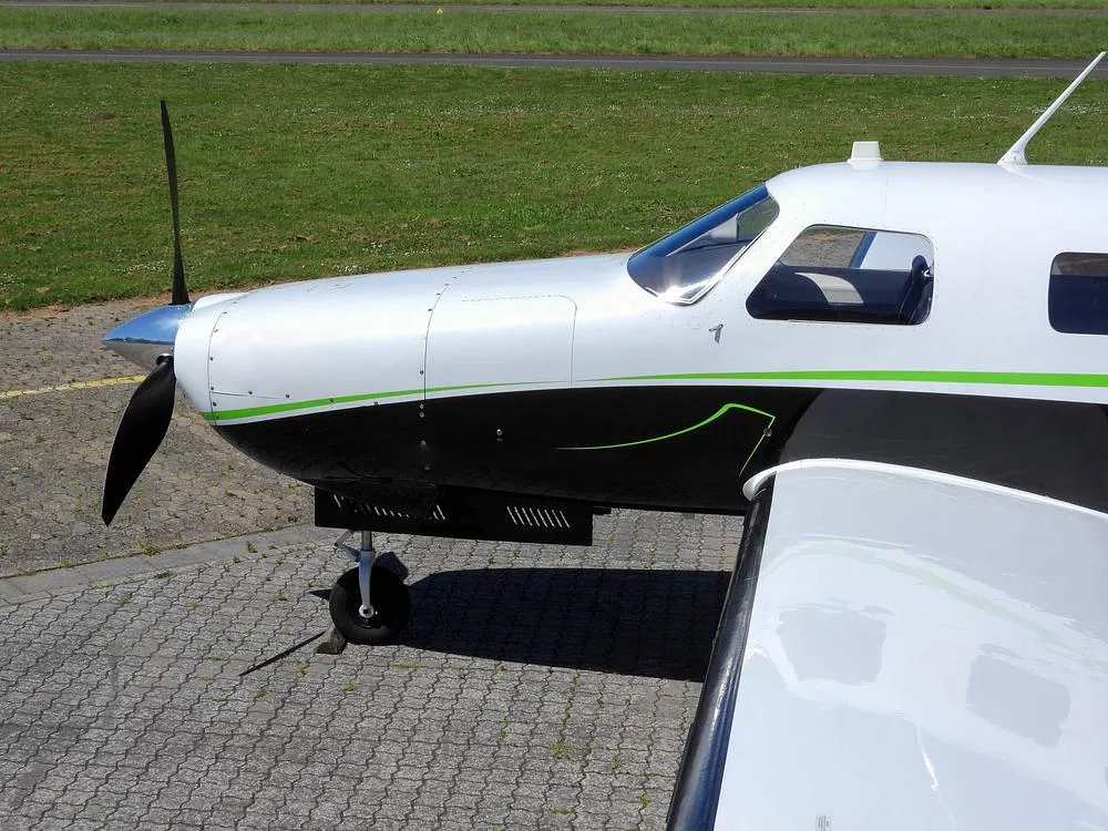 A close-up view of the propeller, nose, and front wing section of a white and black aircraft with green trim.