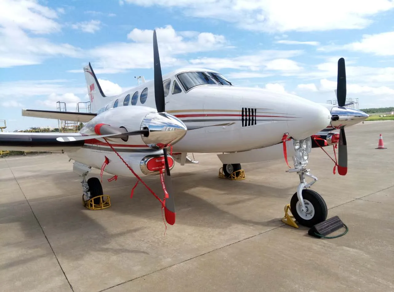 A King Air aircraft is parked on the tarmac with wheel chocks and propeller covers, front quarter view.