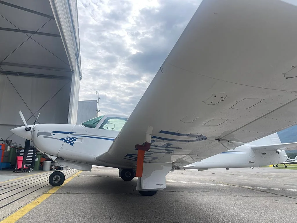 Underside view of the wing of a white single-engine propeller aircraft, parked near a hangar.