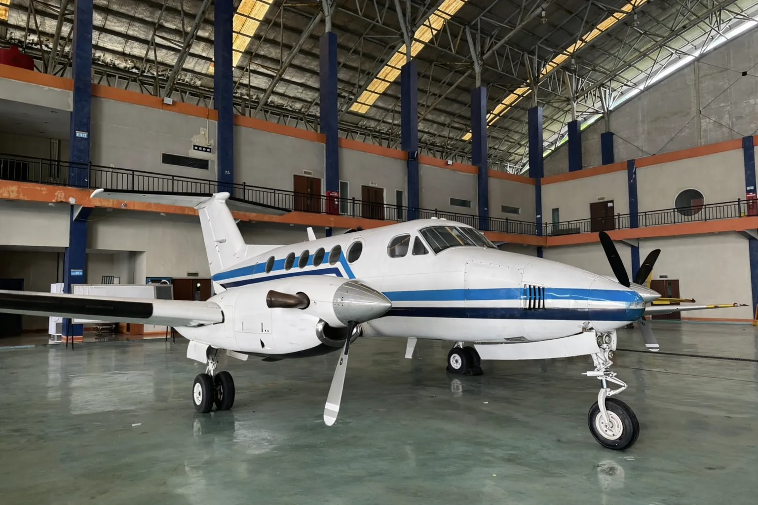 A slightly different three-quarter front view of the white and blue twin-turboprop aircraft in a hangar.