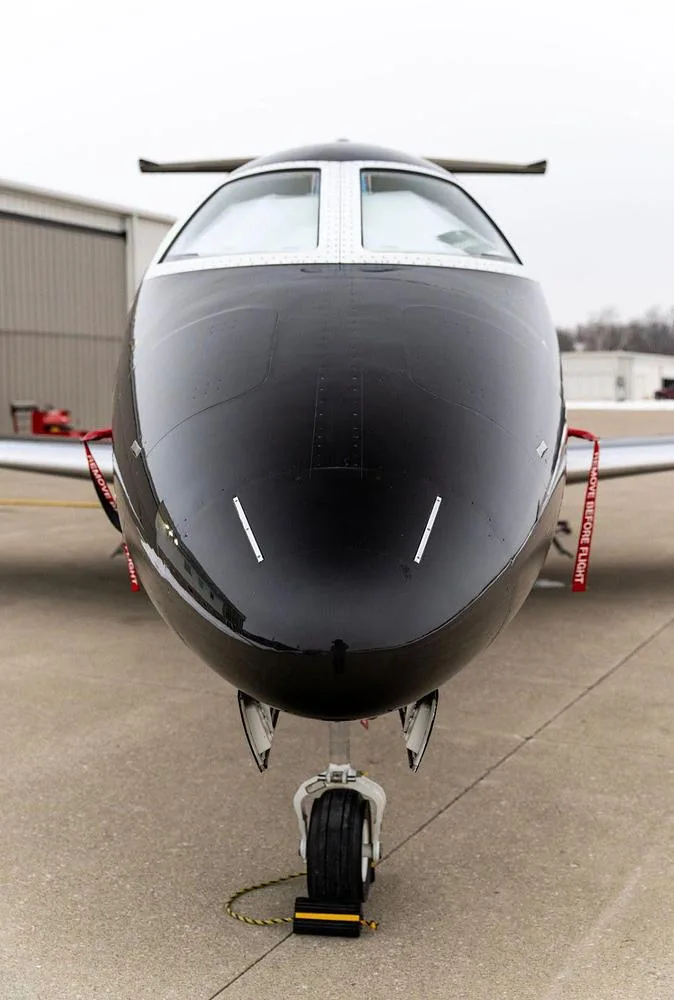A head-on view of the nose and cockpit windows of a black Embraer Phenom 300 jet.