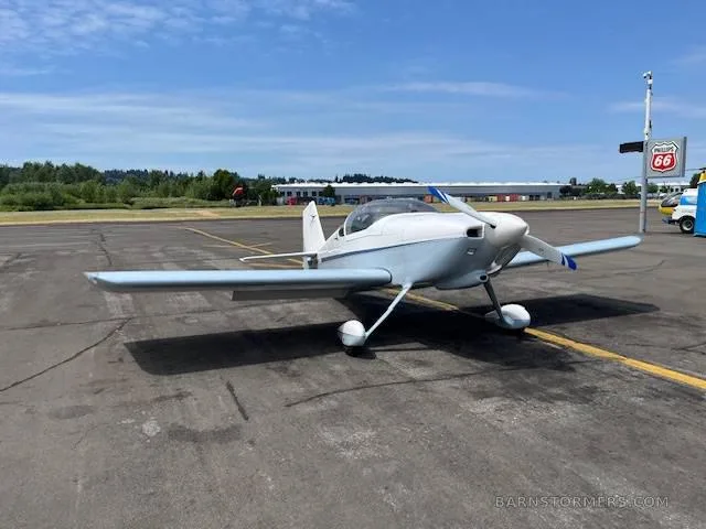 A light blue and white single-engine aircraft with a propeller, parked on an asphalt tarmac under a clear sky.