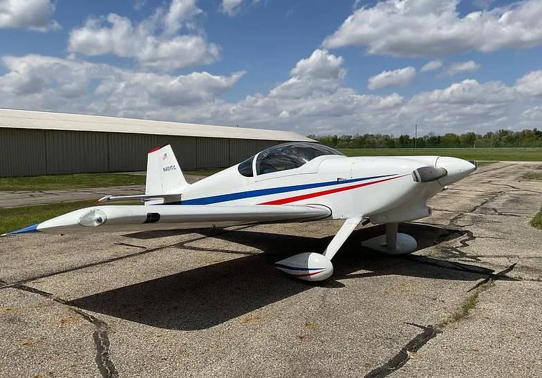 A front-side view of a white single-engine aircraft with red and blue stripes, parked on a tarmac.