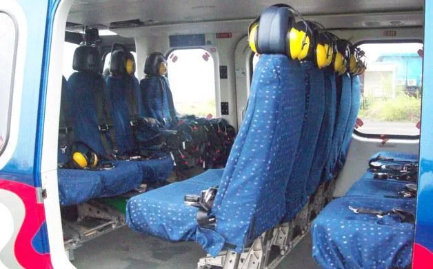 The interior cabin of a helicopter features blue fabric seats with yellow headsets, viewed from the rear.