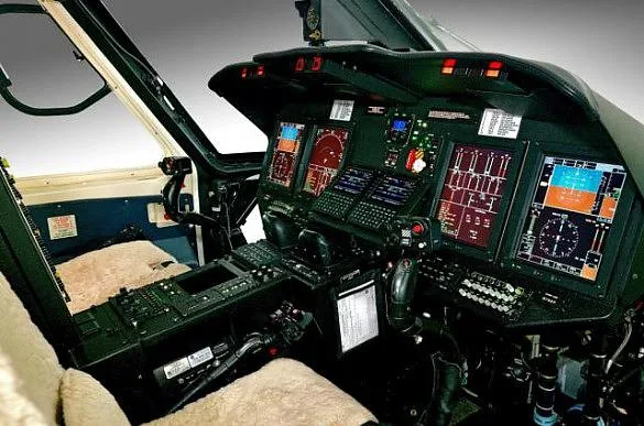 The cockpit of a helicopter featuring multiple digital displays, control sticks, and a central console.