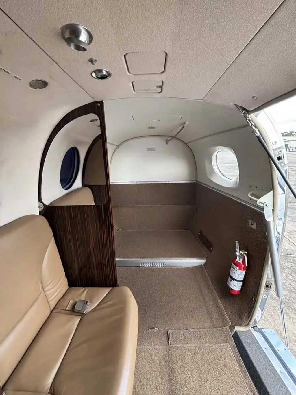The rear interior of the aircraft, showing a cargo area, tan seating, and an open entry door with a fire extinguisher.