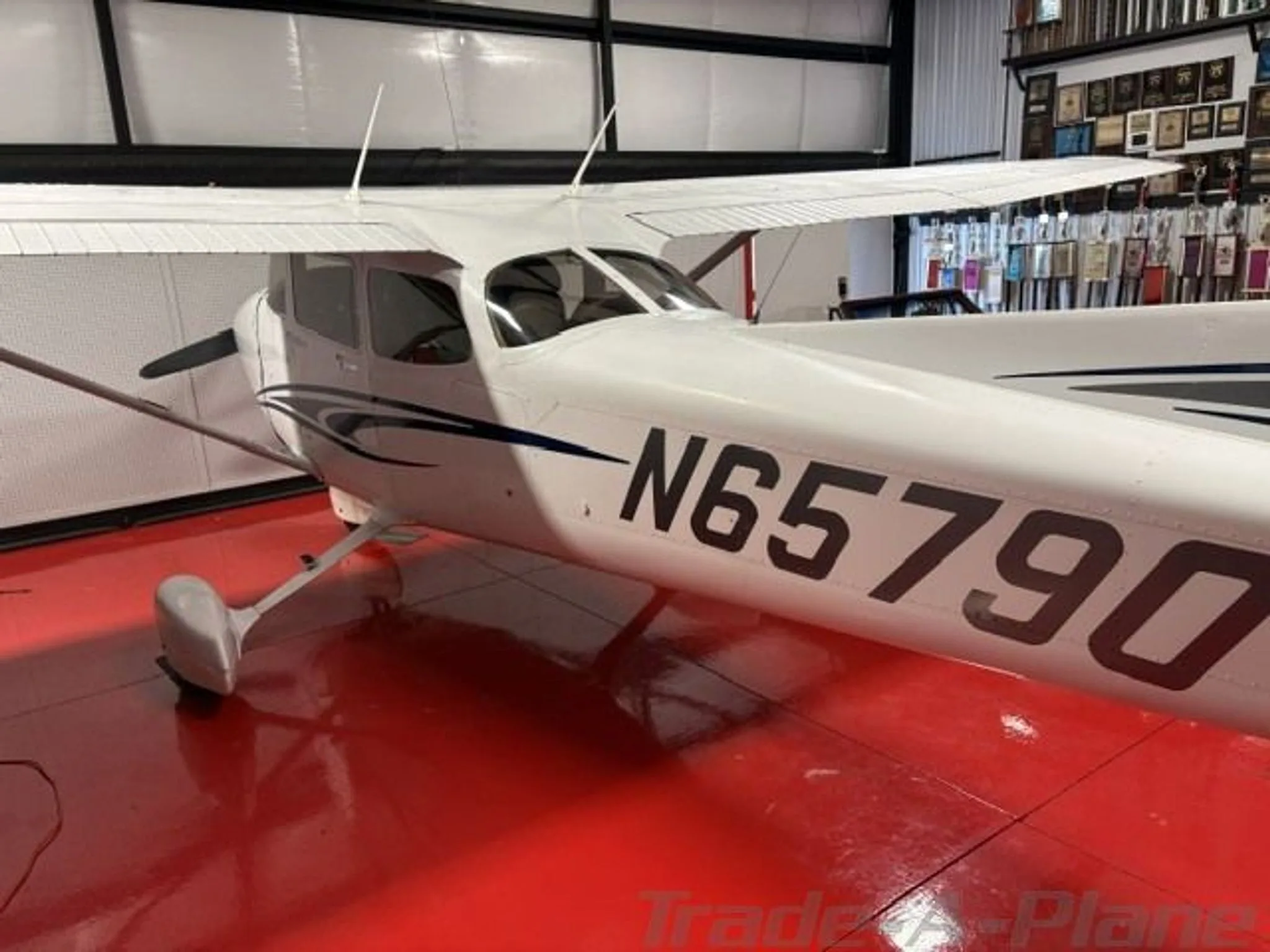 A close-up side view of the white Cessna N65790 with blue and black stripes, parked on a red floor in a hangar.