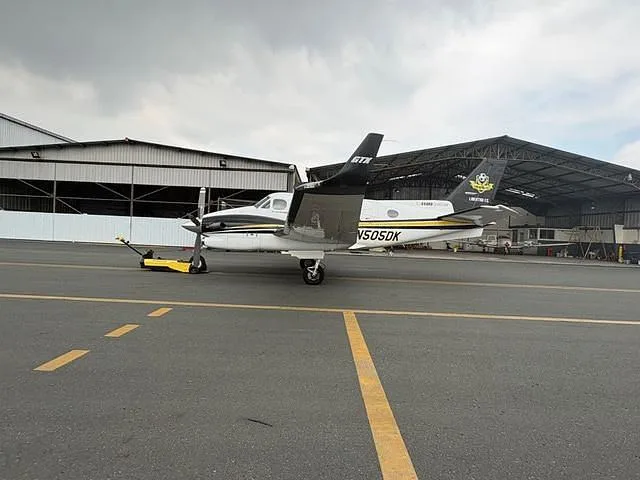 A white and black twin-engine turboprop aircraft with registration N505DK parked on an airfield next to a hangar.