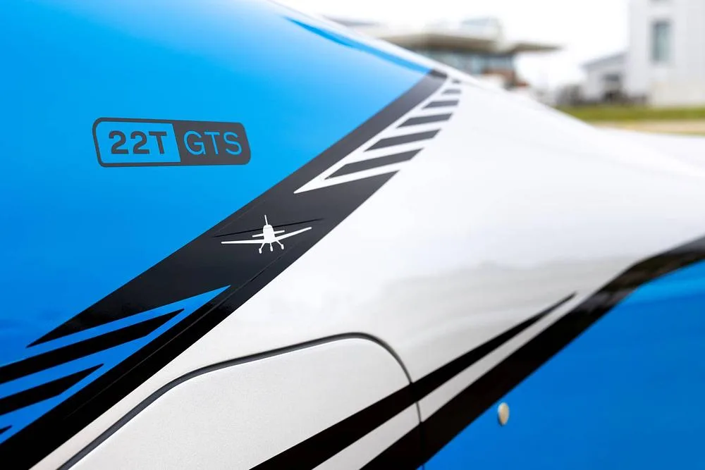A close-up of the blue and silver fuselage of a Cirrus SR22T GTS, showing the "22T GTS" designation and a small aircraft silhouette.