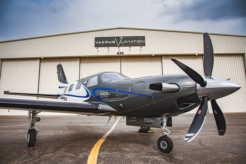 A gray and white HALO equipped aircraft is parked in front of a hangar.