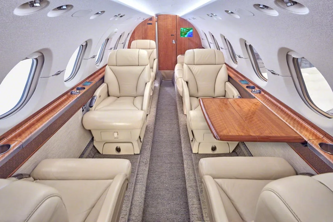 The luxurious interior cabin of a private jet with beige leather seats and polished wood accents.