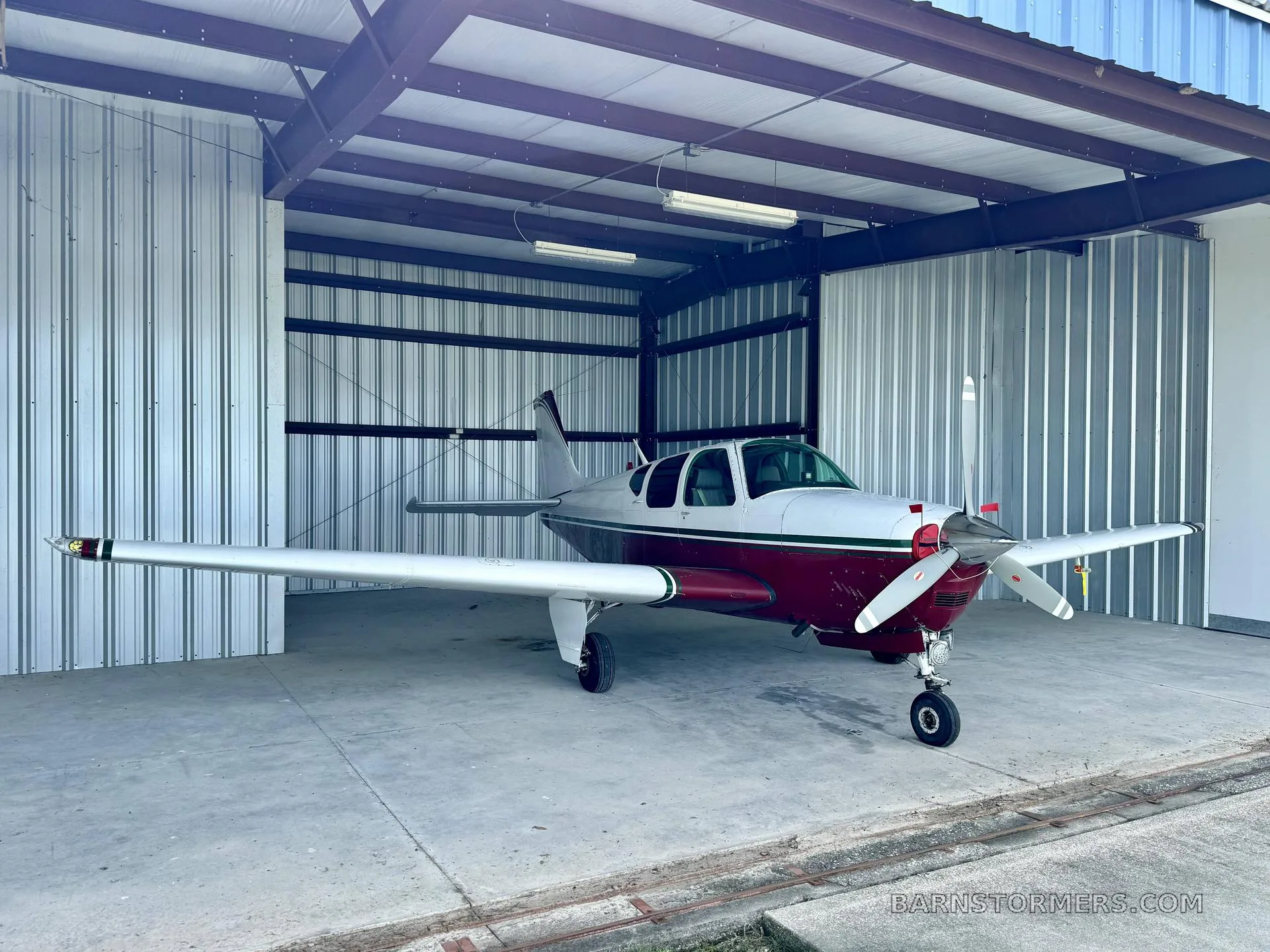 A white and maroon single-engine propeller aircraft is parked inside a metal hangar.