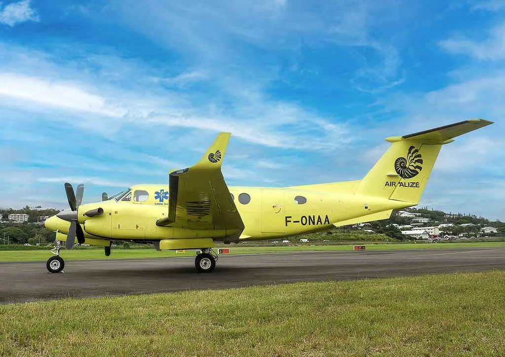 A yellow twin-engine turboprop air ambulance, registration F-ONAA, with "AIR ALIZE" and a spiral logo on the tail, parked on a runway.