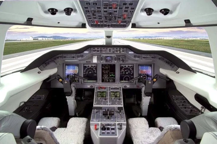 The modern cockpit of a private jet with multiple digital displays and controls, looking out onto a runway.