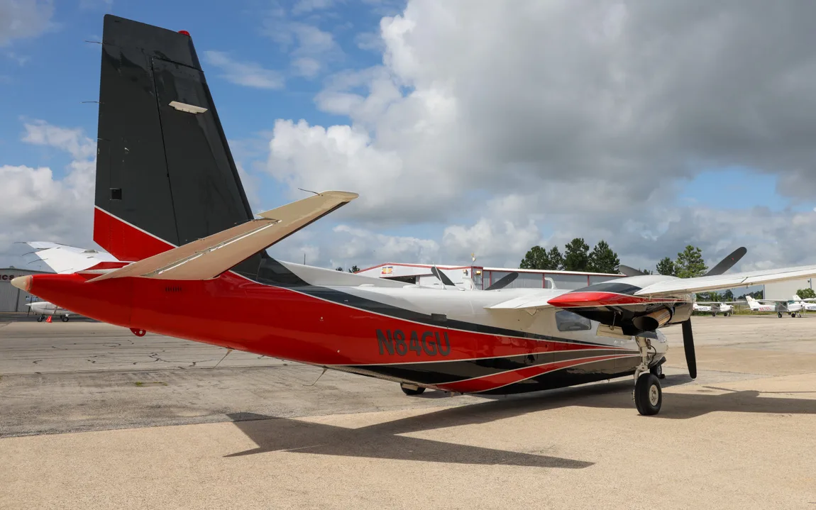 A white, black, and red twin-engine aircraft, N84GU, parked on an tarmac.