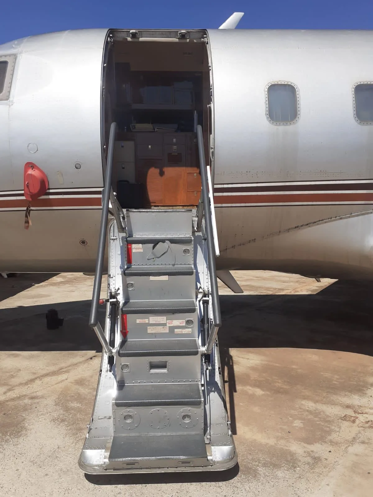 Close-up of the open airstairs leading into the silver fuselage of a business jet, revealing some items inside.