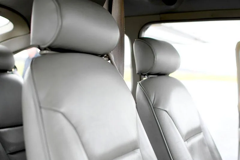 The light gray leather seats of a small aircraft cabin are visible, with a window showing the exterior.