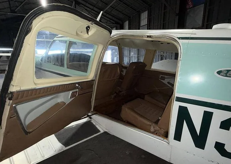 The open passenger door of a Piper Cherokee Six, revealing the brown interior seats.