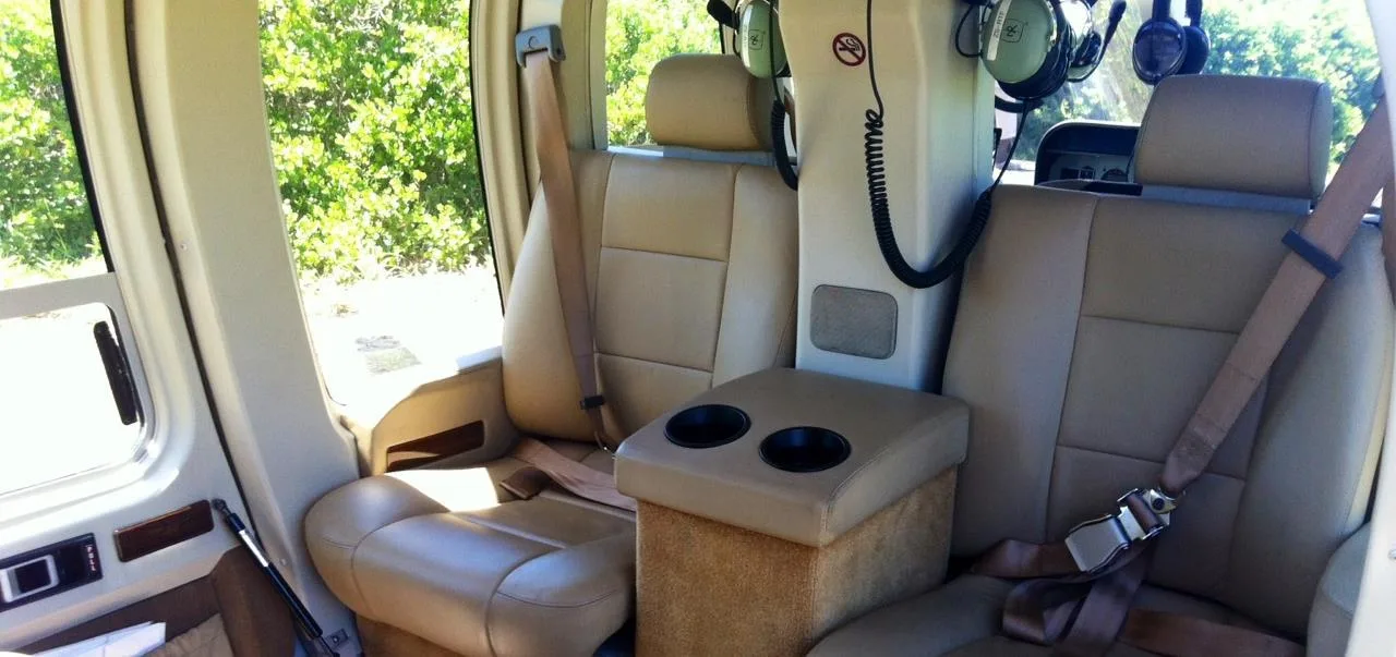 The tan leather interior of a helicopter cabin with two passenger seats and a center console with cup holders.