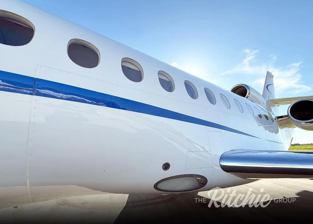 A close-up view of the white Dassault Falcon fuselage with a prominent blue stripe and multiple windows.