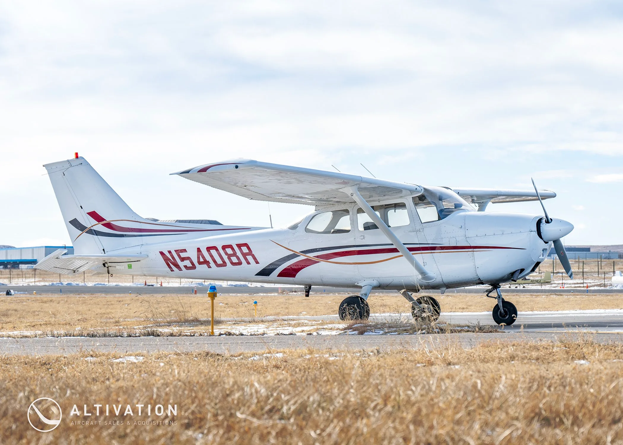 A white Cessna 172 with red and black stripes, registration N5408R, parked on a grassy airfield.