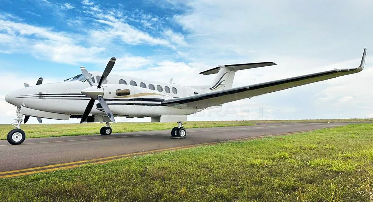 A white Beechcraft King Air 350 with black and gold stripes on a taxiway under a partly cloudy sky.