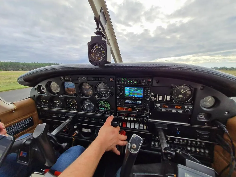 The cockpit of a Piper Archer II on the ground, showing the instrument panel and controls with a cloudy sky outside.