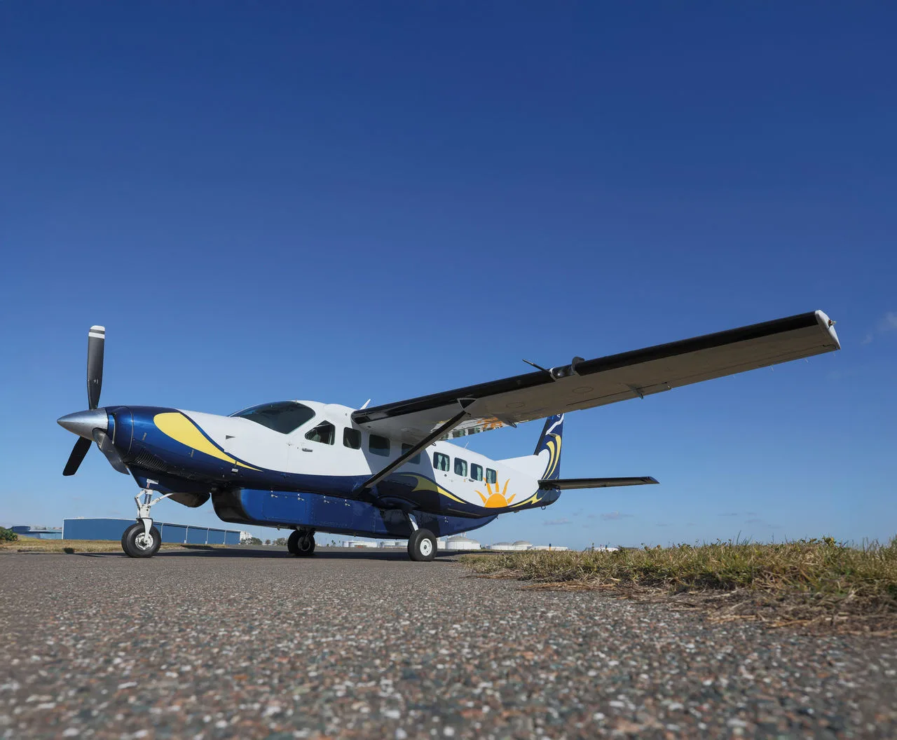 A blue and white turboprop aircraft parked on the tarmac under a clear blue sky.