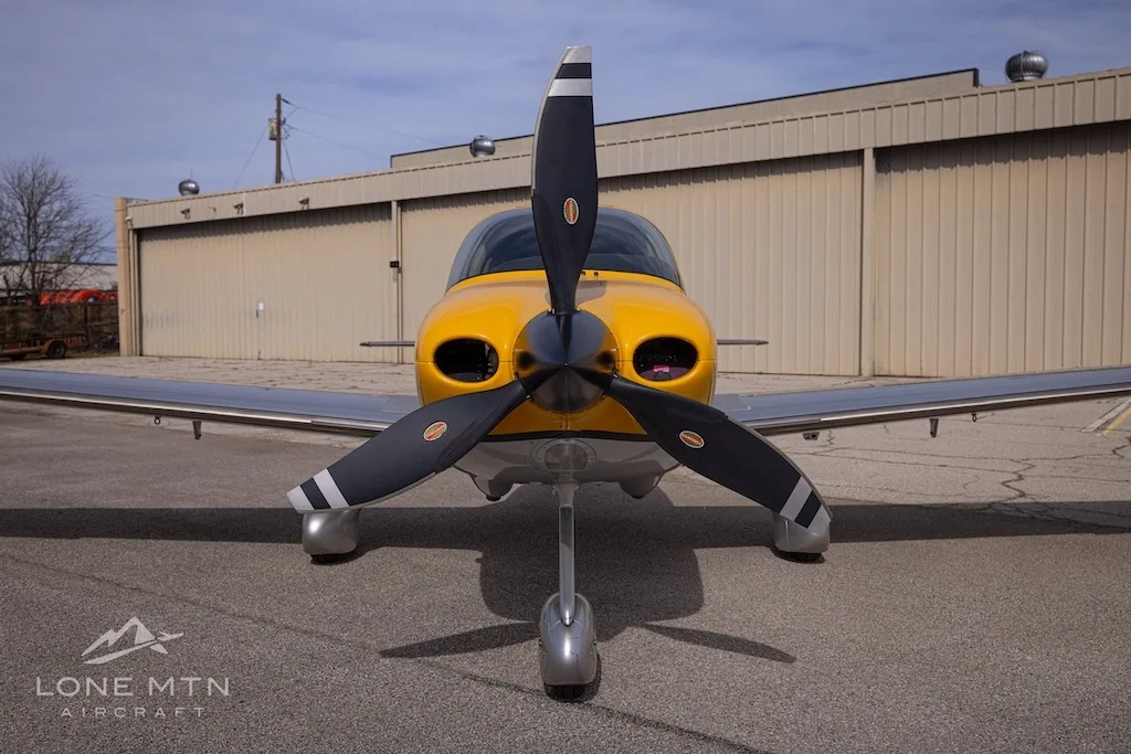 Front view of a Cirrus SR22 aircraft with yellow nose and propeller, parked on an airfield.