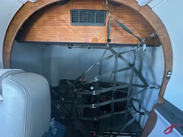An interior view of the aircraft showing a cargo net securing items in the rear cabin area with wood paneling.