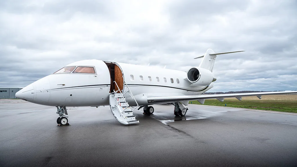 A white business jet with its main cabin door open and airstairs deployed on a tarmac.