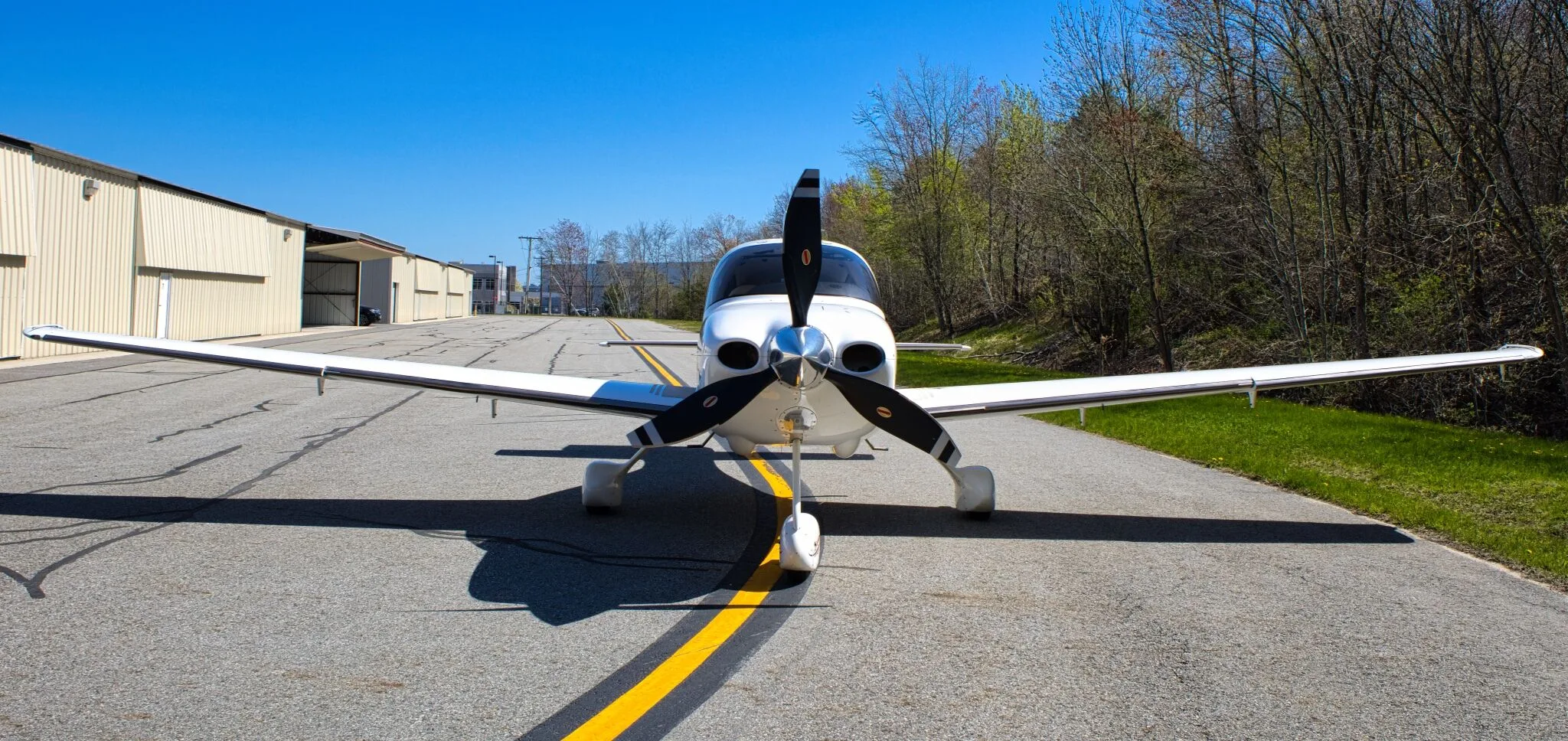 A front view of the white Cirrus SR22 GTS Generation Three aircraft (N459J) with its propeller centered on an airfield.