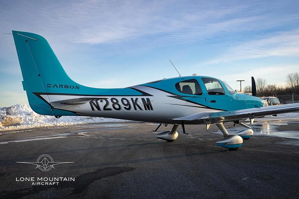 A side view of a turquoise and silver single-engine aircraft, N289KM, on a snowy tarmac.