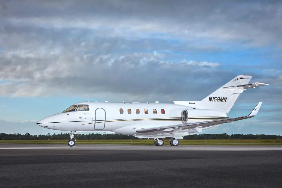 A white business jet with gold and black stripes, tail number N159MN, seen from the side on a tarmac.